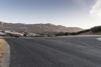 a man riding a skateboard across an empty street in the mountains with some trees and grass