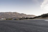 a man riding a skateboard across an empty street in the mountains with some trees and grass