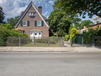 an old brick home with lots of greenery in front of it and the gate is locked to the road