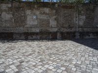 an old brick wall with a blue sign on the back of it in the middle of a paved street