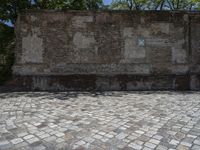 an old brick wall with a blue sign on the back of it in the middle of a paved street