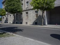 this is an old building on a street corner next to a road with trees and bushes on either side