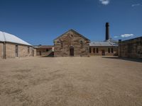 an old building with two chimneys and a round entrance in a dirt courtyard with white trim