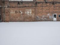 an old building with graffiti on the wall next to snow in wintertime near city street