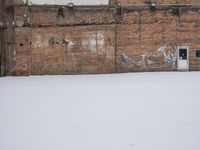 an old building with graffiti on the wall next to snow in wintertime near city street