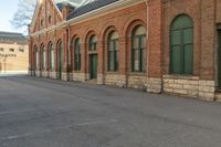 an old building with arches on the roof and two green windows along the wall, and another half way of the road is empty