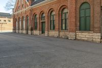 an old building with arches on the roof and two green windows along the wall, and another half way of the road is empty