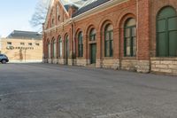 an old building with arches on the roof and two green windows along the wall, and another half way of the road is empty