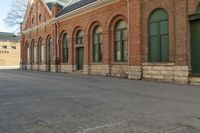 an old building with arches on the roof and two green windows along the wall, and another half way of the road is empty