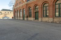 an old building with arches on the roof and two green windows along the wall, and another half way of the road is empty