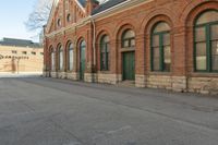 an old building with arches on the roof and two green windows along the wall, and another half way of the road is empty