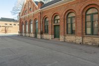 an old building with arches on the roof and two green windows along the wall, and another half way of the road is empty