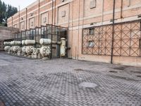 several large steel pipes standing in front of an old building with brick walls and a gate
