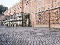 several large steel pipes standing in front of an old building with brick walls and a gate