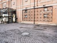 several large steel pipes standing in front of an old building with brick walls and a gate