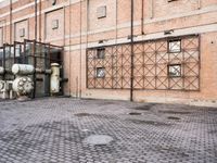 several large steel pipes standing in front of an old building with brick walls and a gate