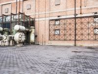 several large steel pipes standing in front of an old building with brick walls and a gate