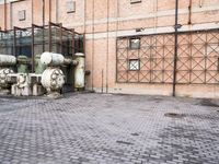 several large steel pipes standing in front of an old building with brick walls and a gate
