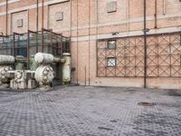 several large steel pipes standing in front of an old building with brick walls and a gate