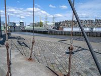 some old fashioned metal pole on the road near water and a city and waterfront area