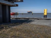 an old yellow and red fire hydrant at a port entrance with a large boat out in the distance