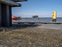 an old yellow and red fire hydrant at a port entrance with a large boat out in the distance