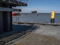 an old yellow and red fire hydrant at a port entrance with a large boat out in the distance