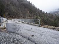 an old railroad bridge is partially over and over the road in the mountains on a cloudy day