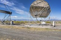 an old satellite mirror sitting on top of a dirt field near a blue sky and grass