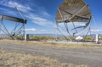 an old satellite mirror sitting on top of a dirt field near a blue sky and grass