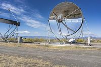 an old satellite mirror sitting on top of a dirt field near a blue sky and grass