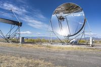 an old satellite mirror sitting on top of a dirt field near a blue sky and grass