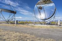 an old satellite mirror sitting on top of a dirt field near a blue sky and grass