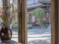 a house that is outside from inside a window with a vase on the counter next to it