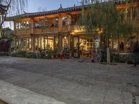 people are walking around outside an old building with shops and stores behind them at dusk