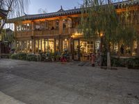 people are walking around outside an old building with shops and stores behind them at dusk