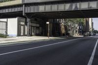 an old train bridge over the road near some buildings in a city area, a man riding a skateboard