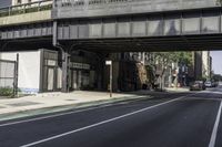 an old train bridge over the road near some buildings in a city area, a man riding a skateboard