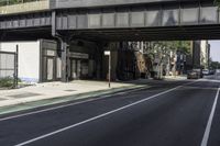 an old train bridge over the road near some buildings in a city area, a man riding a skateboard