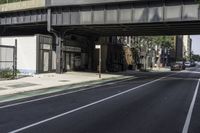 an old train bridge over the road near some buildings in a city area, a man riding a skateboard