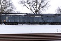 a large old train is going past several trees on the snowy ground near a wooden bench