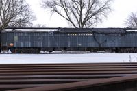 a large old train is going past several trees on the snowy ground near a wooden bench