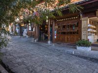 a stone street with plants and shops on either side of the road near a tree