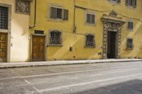 an old yellow building is on the side of the street and there are two windows, and a bicycle parked near it