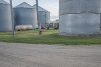 an older man riding down the road in front of large silo like buildings on a farm