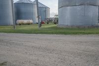 an older man riding down the road in front of large silo like buildings on a farm
