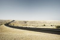 an asphalt road leading through the desert on a clear day with a mountain in the distance