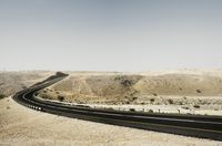 an asphalt road leading through the desert on a clear day with a mountain in the distance