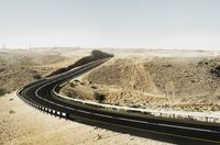 an asphalt road leading through the desert on a clear day with a mountain in the distance