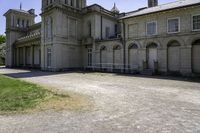 an old stone building that has grass on the outside and in front of it, next to a white fence and bushes